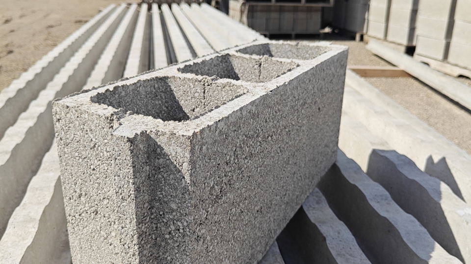 Een close-up van een betonnen sintelblok dat op een stapel golfplaten, renovatievloeren en vulstenen ligt op een bouwmaterialenopslagplaats in de open lucht.