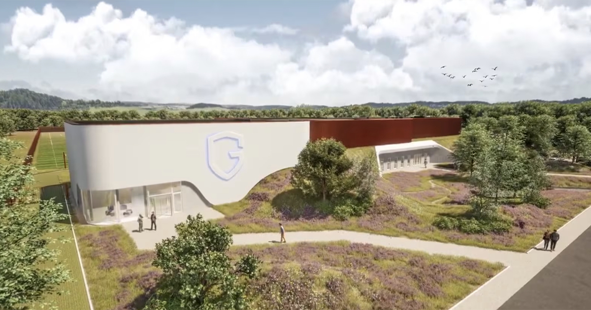 A modern building with a curved design and large windows is surrounded by landscaped greenery and paths. A logo with the letter "G" is displayed on the front. People are walking outside.